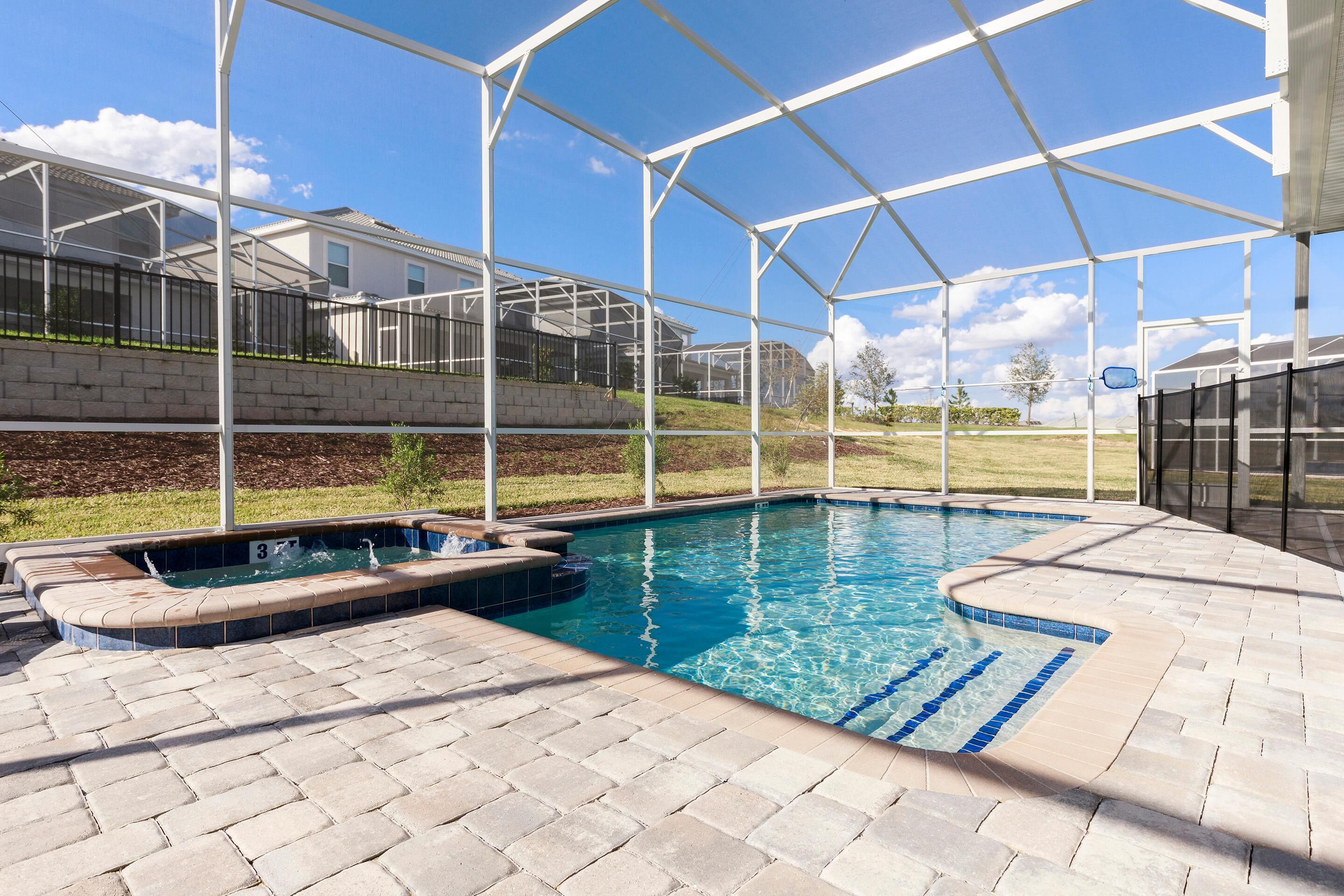 A swimming pool with a sunken hot tub, surrounded by a covered patio area with a view of a residential neighborhood.