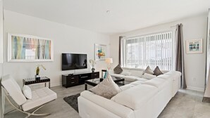 A modern living room with a white sofa, a white rocking chair, a flat-screen TV, and artwork on the walls. - 1559fd - The Retreat at Championsgate (Davenport)