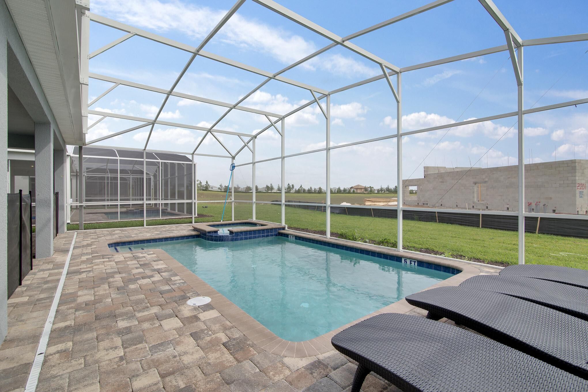 A covered outdoor swimming pool with a brick patio and lounge chairs.