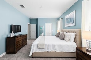 A bedroom with a bed, dresser, TV, and artwork on the wall.