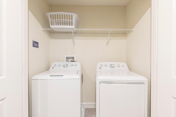 A laundry room with two white front-loading washing machines and a white laundry basket on a shelf.