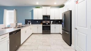 Una cocina moderna con armarios blancos, un refrigerador negro, un microondas y un lavavajillas.