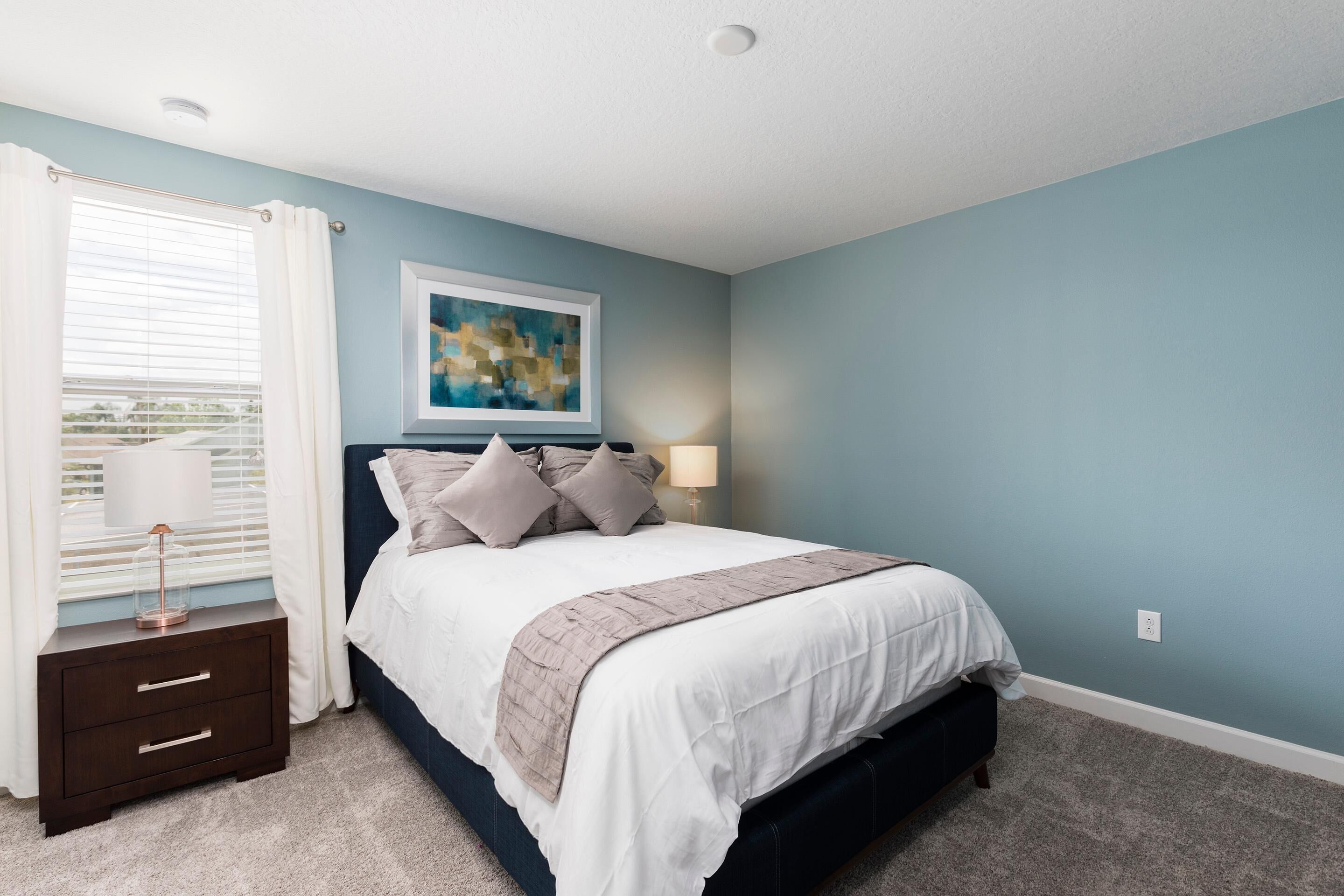 A bedroom with a bed, nightstand, lamp, and a painting on the wall.