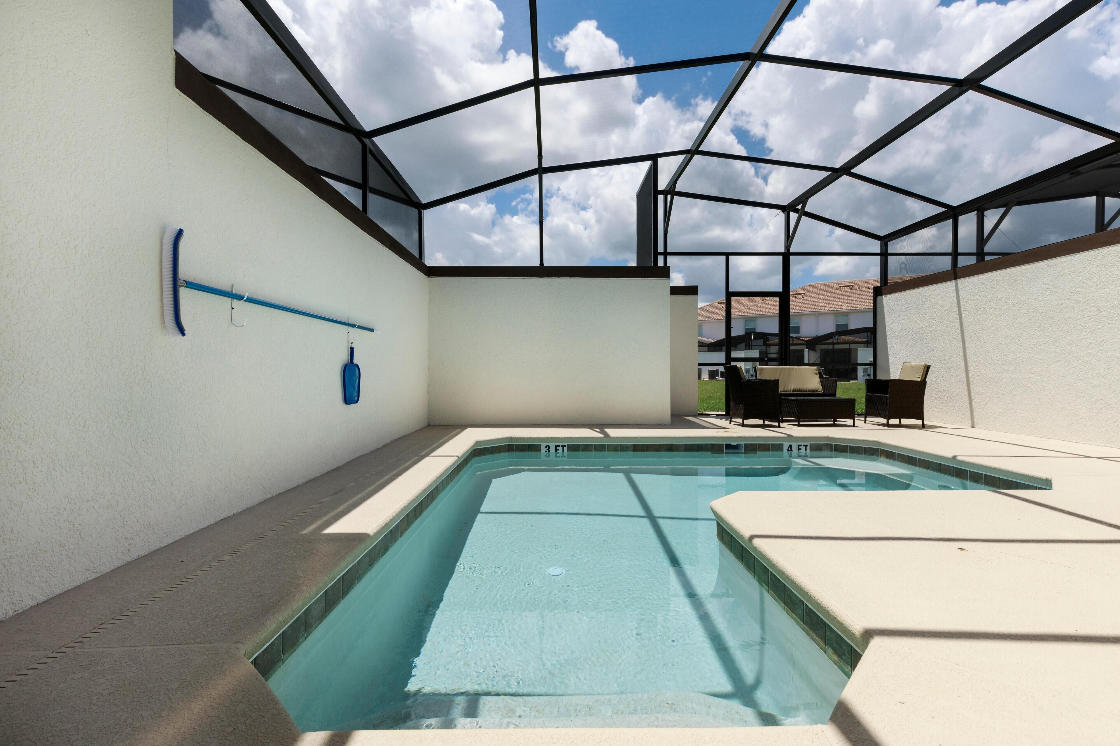 A swimming pool with a glass ceiling, surrounded by a white wall and a tiled deck.