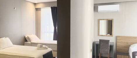 A hotel room with a bed, a desk, a chair, a mirror, and an air conditioning unit.