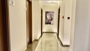 Um corredor com piso de mármore, portas em ambos os lados e um quadro na parede do fundo.