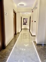 Un pasillo con suelo de mármol, puertas a ambos lados y un cuadro al fondo.