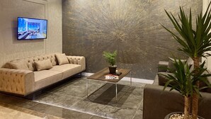 Uma sala de estar moderna com um sofá, uma mesa de centro, uma televisão e um detalhe decorativo na parede.