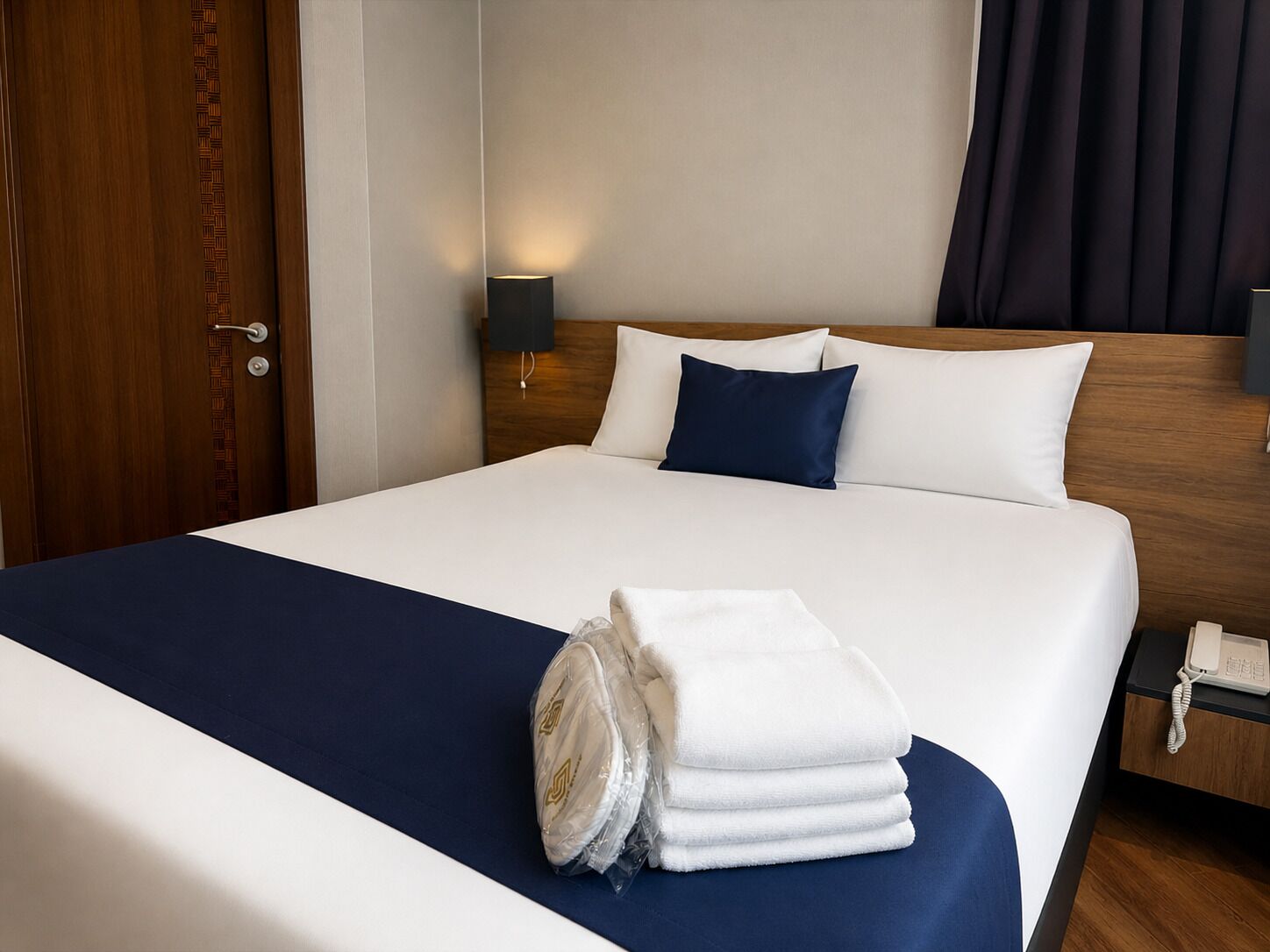 A hotel room with a neatly made bed, a bedside lamp, a telephone, and a door with a patterned design.