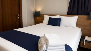 A hotel room with a neatly made bed, a bedside lamp, a telephone, and a door with a patterned design.