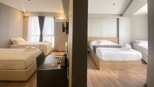 Quarto de hotel moderno com duas camas, uma escrivaninha com um laptop, máquina de café e TV na parede.