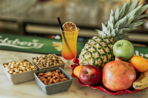 Une table avec un ananas, une grenade, une pomme, une orange et un verre contenant une boisson, avec une paille.