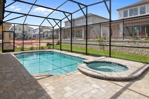 Une piscine avec un jacuzzi, entourée d’une terrasse en briques et d’une clôture en métal.