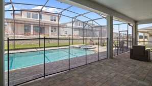 En overdækket terrasse med swimmingpool, udsigt til nærliggende huse og udendørs møbler.
