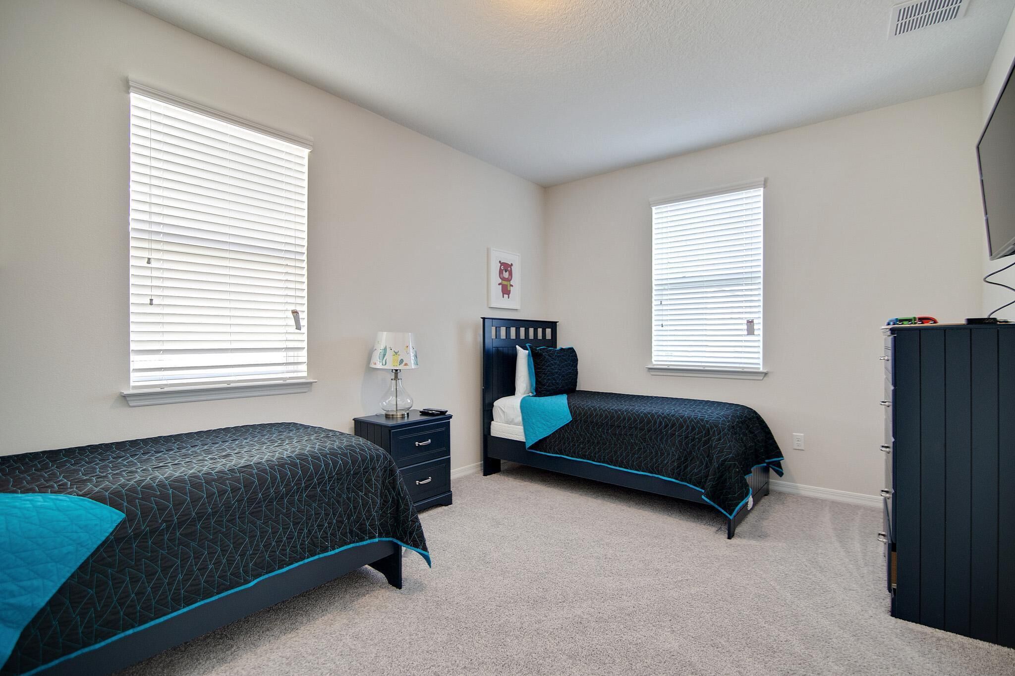 A bedroom with two beds, a nightstand, a dresser, and a TV.