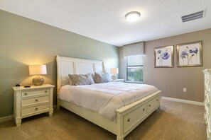 A bedroom with a white bed, two bedside tables with lamps, a nightstand, and two framed floral pictures on the wall.