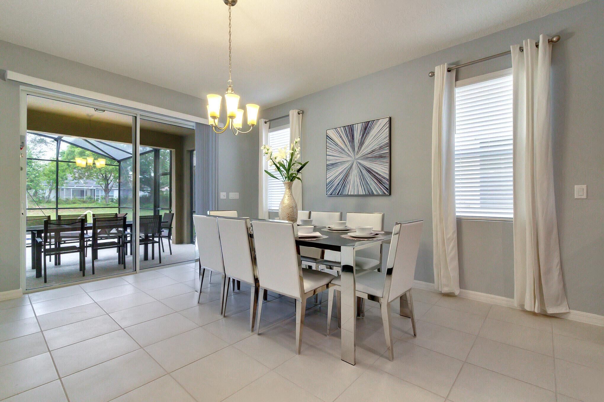 A dining area with a table set for four, chairs, a chandelier, and a vase with flowers.