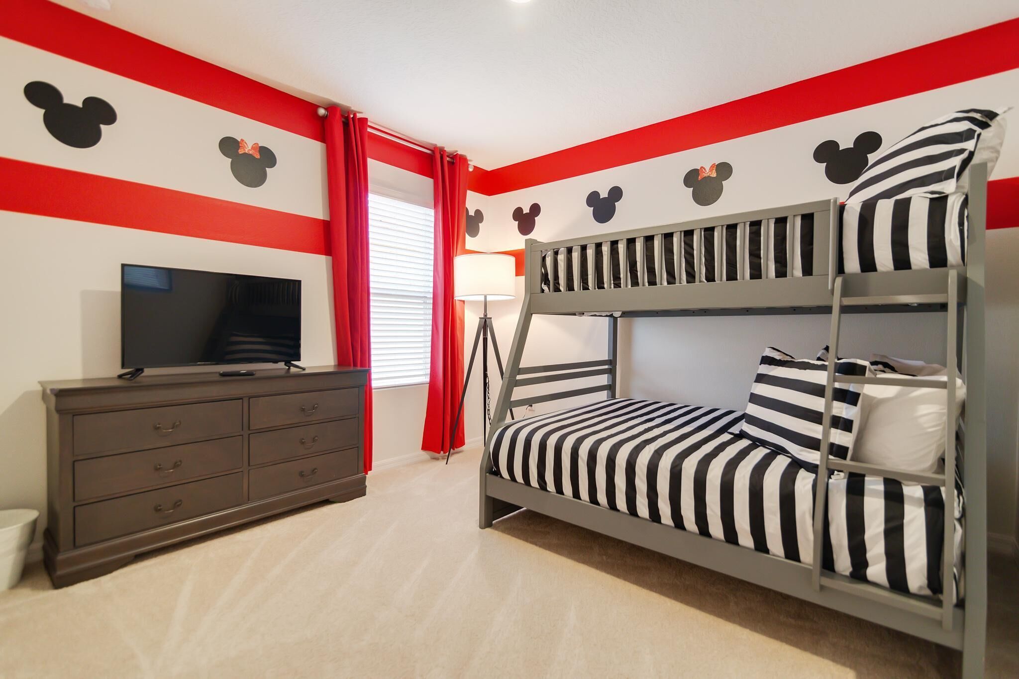 A bunk bed with striped bedding, a television on a dresser, and Mickey Mouse wall decals.