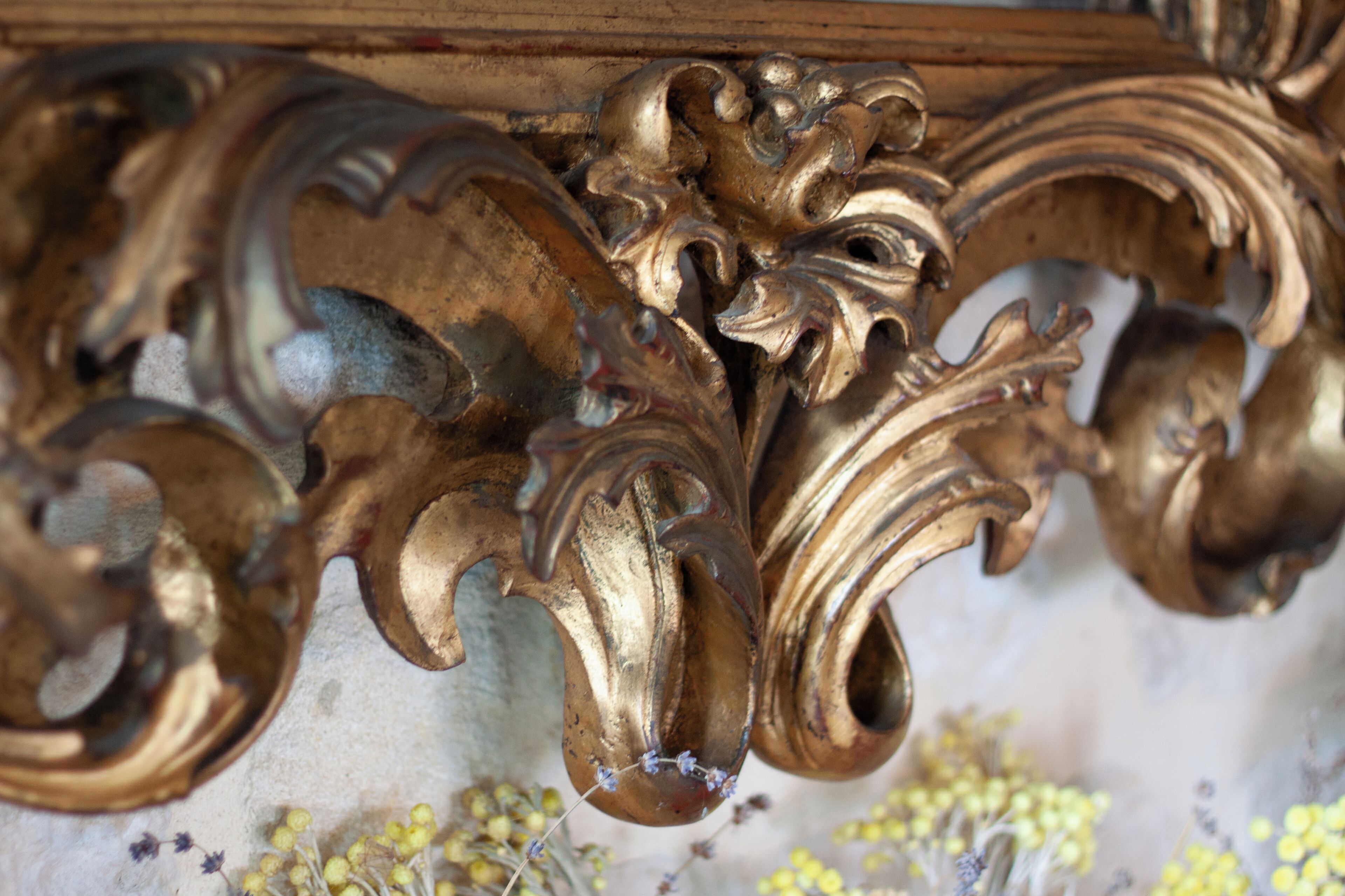Detalle de metal dorado muy ornamentado con diseños intrincados, probablemente parte de un mueble o elemento arquitectónico.
