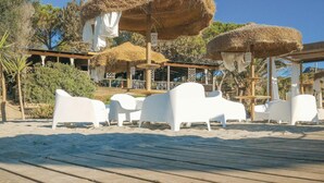 Un complexe hôtelier en bord de mer, doté de parasols en chaume, de chaises longues blanches et d’une terrasse en bois.
