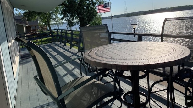 Une terrasse couverte avec une table ronde et des chaises, donnant sur une étendue d’eau où flotte un drapeau américain.