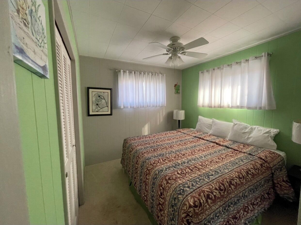 Ein Schlafzimmer mit einem Bett, einem Deckenventilator und einem Fenster mit Vorhängen.