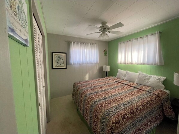 A bedroom with a bed, a ceiling fan, and a window with curtains.