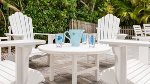 A white outdoor seating area with a round table, surrounded by white chairs, and a blue pitcher with floral designs.