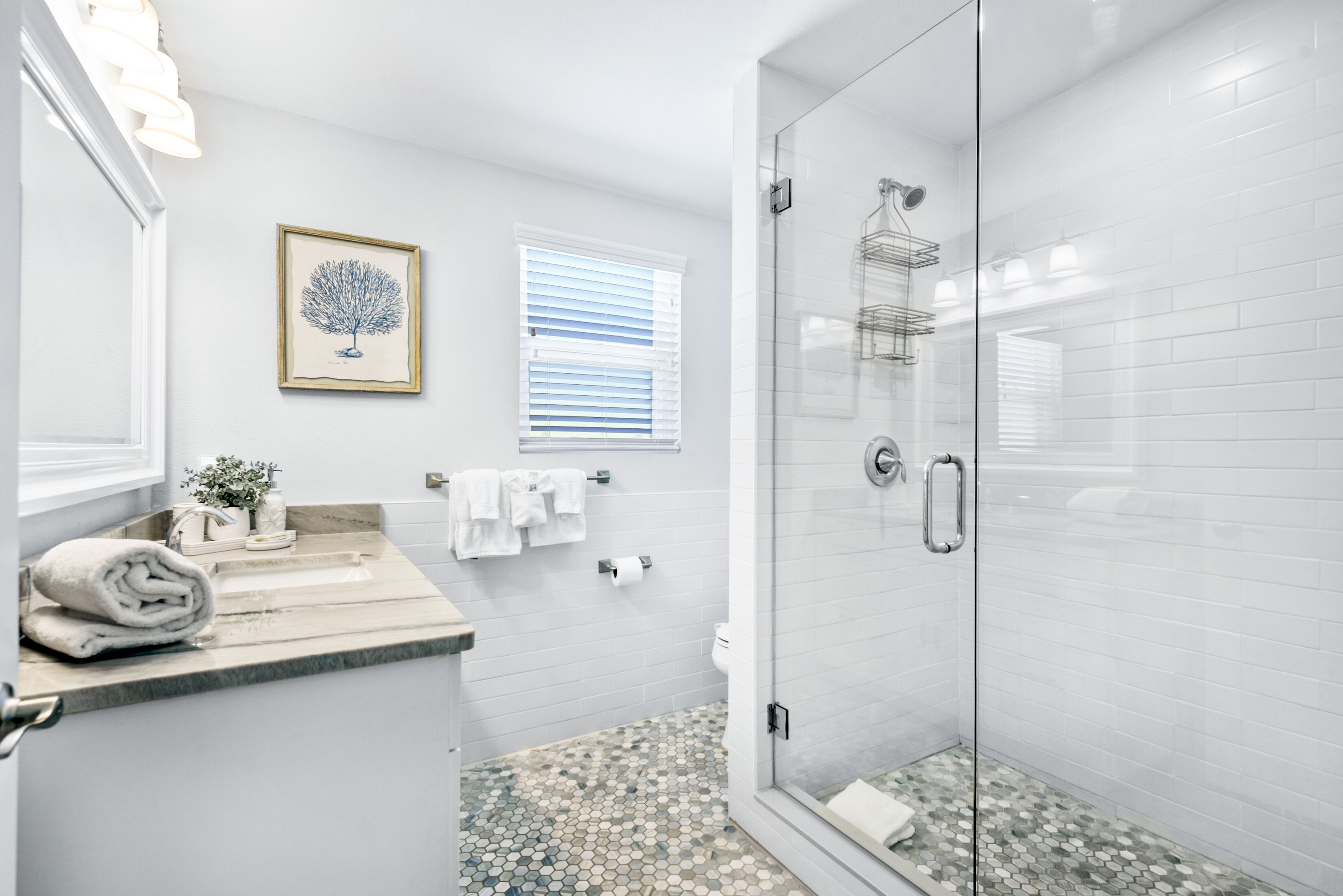 Une salle de bain moderne avec une douche à parois de verre, un comptoir en marbre et une œuvre d’art encadrée au mur.