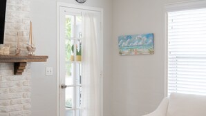 A room with a white brick wall, a white door with a window, a white sofa, and a painting of a beach scene.
