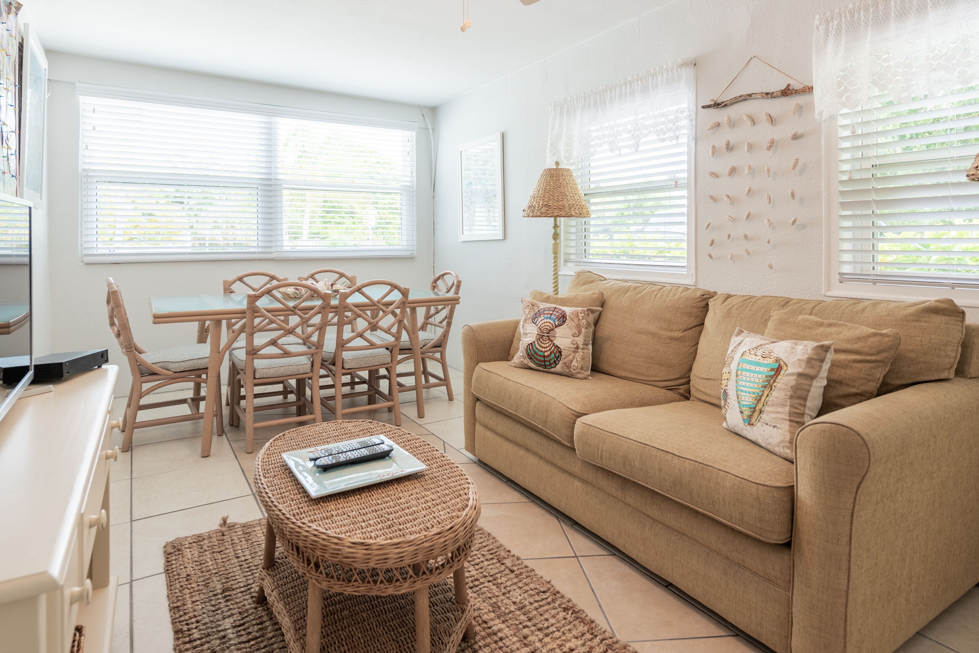 A living room with a beige sofa, a coffee table, wicker chairs, a dining table, and a TV.