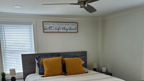 A bedroom with a bed, a ceiling fan, a bedside table with a lamp, a nightstand, and a window with blinds. - Conveniently Located Downtown Apartment (Atlanta)