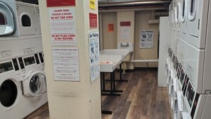 A laundry facility with multiple washing machines and dryers, wooden flooring, and various instructional signs. - Conveniently Located Downtown Apartment (Atlanta)