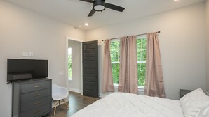 A bedroom with a bed, a dresser, a chair, a ceiling fan, and a window with curtains.