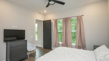 A bedroom with a bed, a dresser, a chair, a ceiling fan, and a window with curtains.