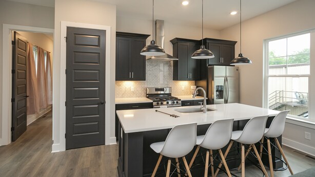 A modern kitchen with dark cabinets, a large island, pendant lighting, and a view to the outside.
