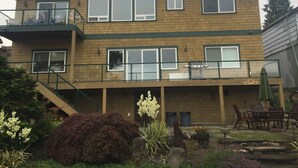 Une maison en bois à deux étages, dotée d’un balcon, d’un porche avec du mobilier d’extérieur et d’un petit jardin.