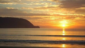 Un coucher de soleil sur une plage, avec des vagues calmes et une formation terrestre visible au loin.