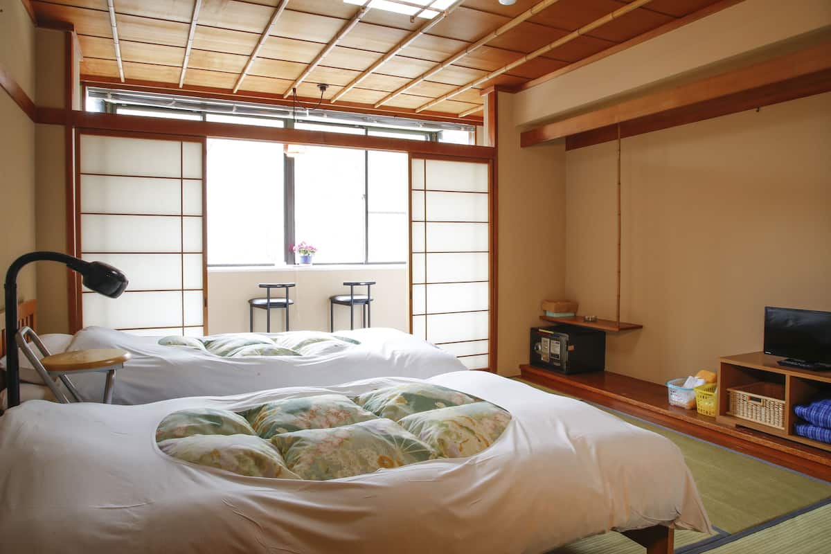 A traditional Japanese-style room with tatami flooring, two beds with floral bedding, a television, and a sliding door leading to a balcony.