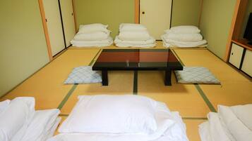 A tatami mat room with a low table, pillows, and a television on a cabinet.