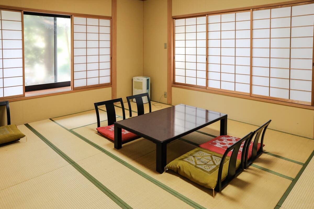 A tatami mat room with a low table, chairs, and a traditional sliding door.