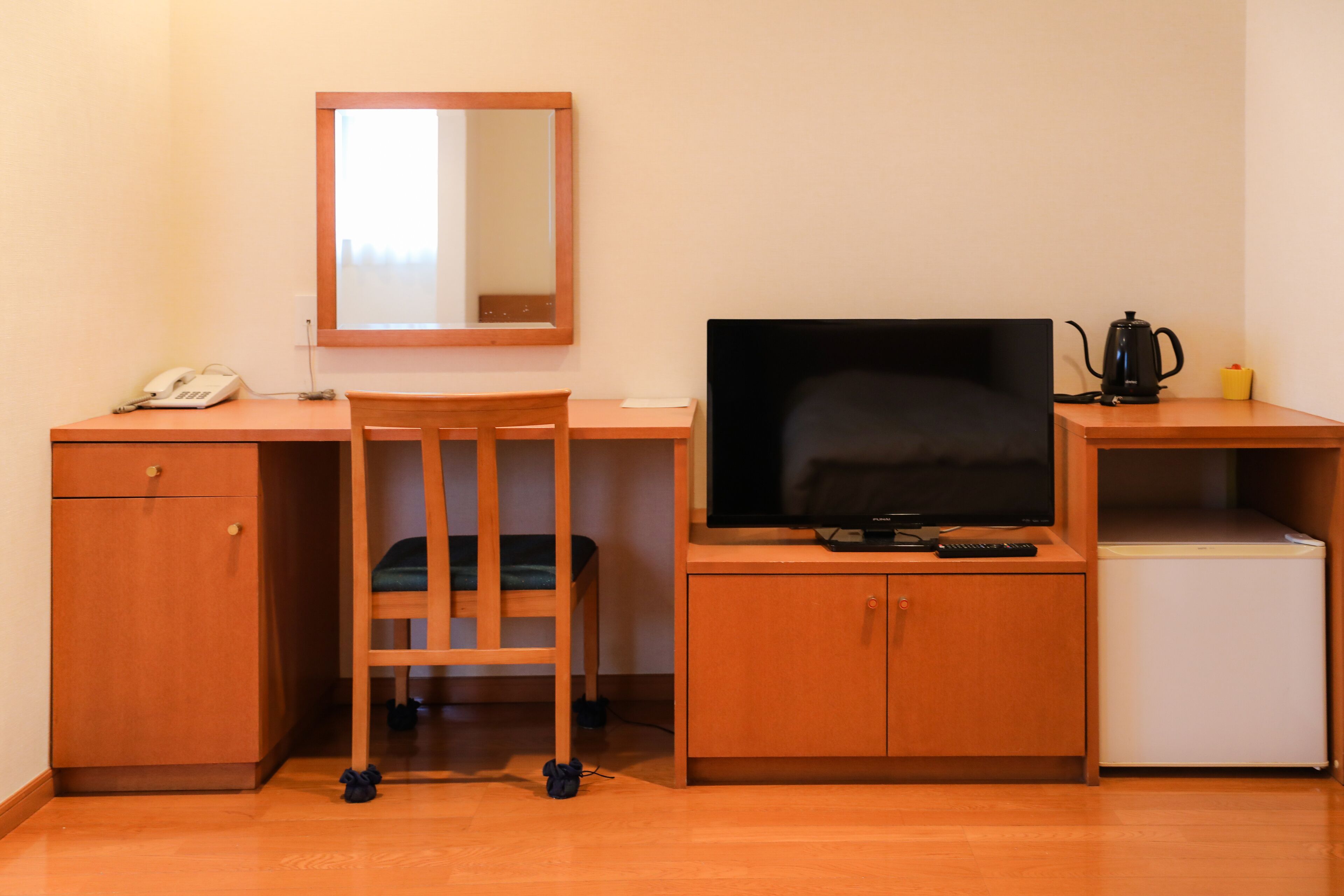 Une chambre d’hôtel équipée d’un bureau en bois, d’une télévision, d’un petit réfrigérateur, d’une machine à café et d’une chaise.