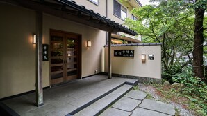 Perinteinen japanilainen rakennus, jossa on puuovi ja kivestä tehdyt portaat, jotka johtavat laatoitetulle sisäänkäynnille.