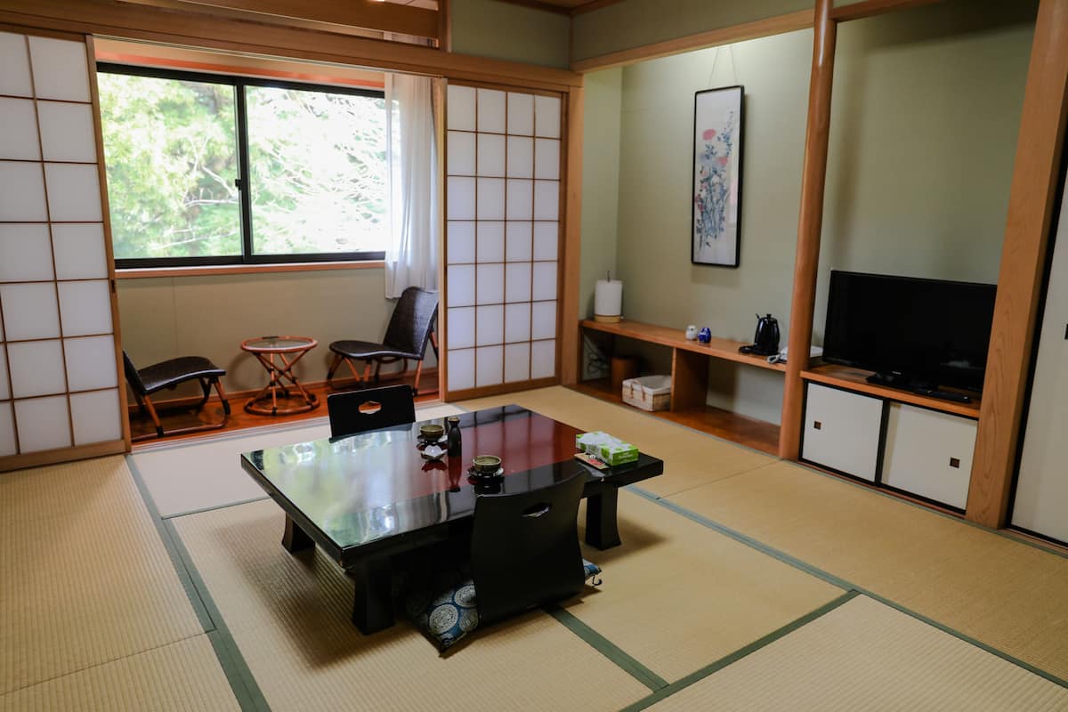 A traditional Japanese room with tatami flooring, a low table with chairs, a television, and a sliding door.