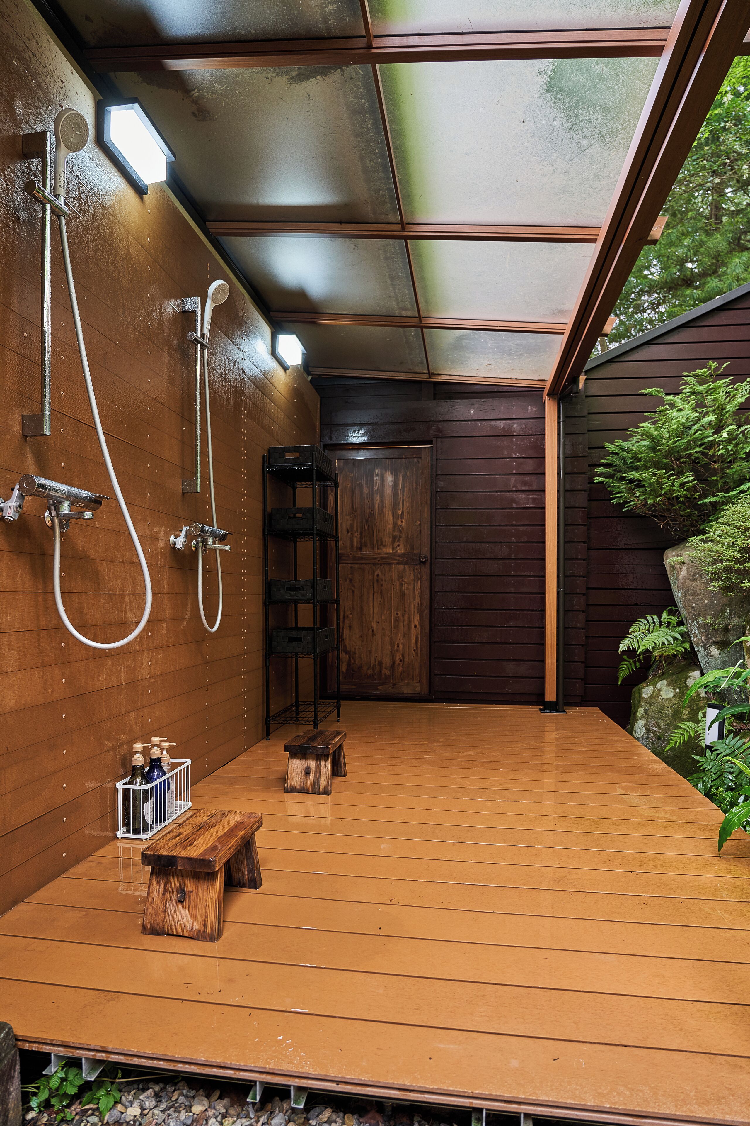 A wooden deck with a built-in shower area, wooden benches, and a door leading to an interior space.