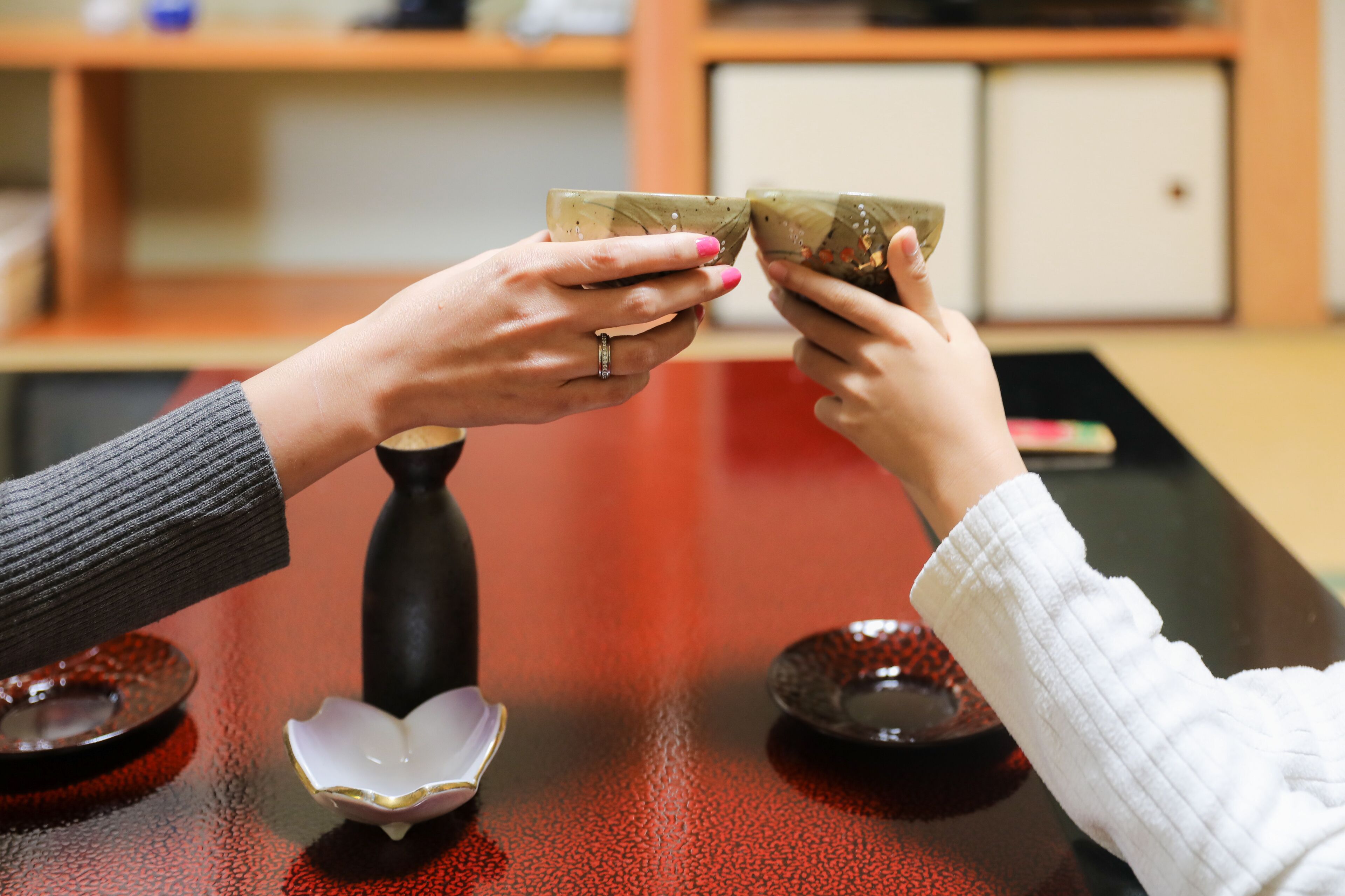 Two hands holding a cup, a small bowl, and a spoon on a table.