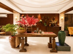 Um hall amplo com uma recepção de madeira, um vaso grande de flores e um vaso decorativo verde.