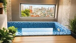 Ein modernes Badezimmer mit großem Fenster, einer blauen Wannentasse und Blick auf die Stadt.