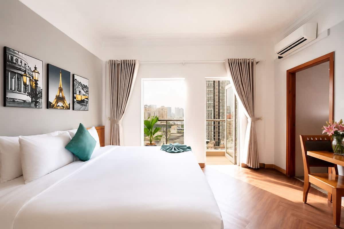 Une chambre d’hôtel avec un grand lit, un bureau, une chaise, une plante en pot et une vue sur le paysage urbain.