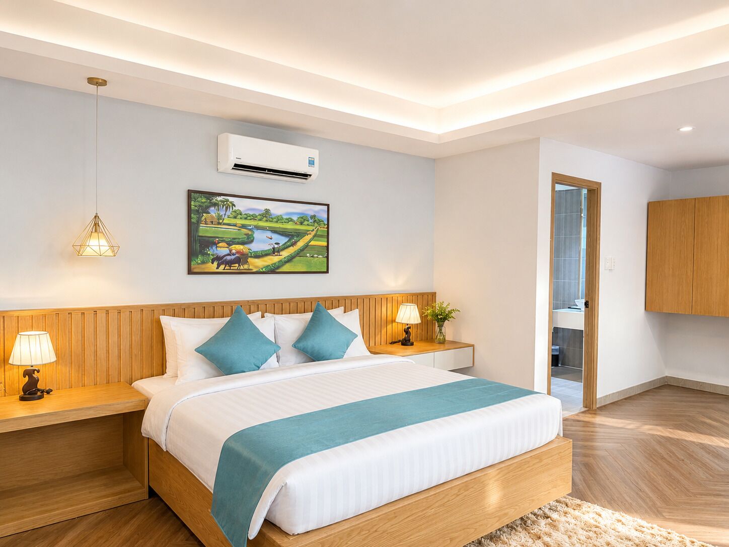 Une chambre d’hôtel moderne avec un lit en bois, deux tables de chevet avec des lampes, un climatiseur fixé au mur et un tableau représentant un paysage.